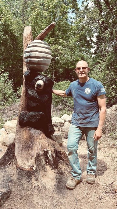 Black bear climbing to a beehive, carved from an oak stump, with Mike for scale